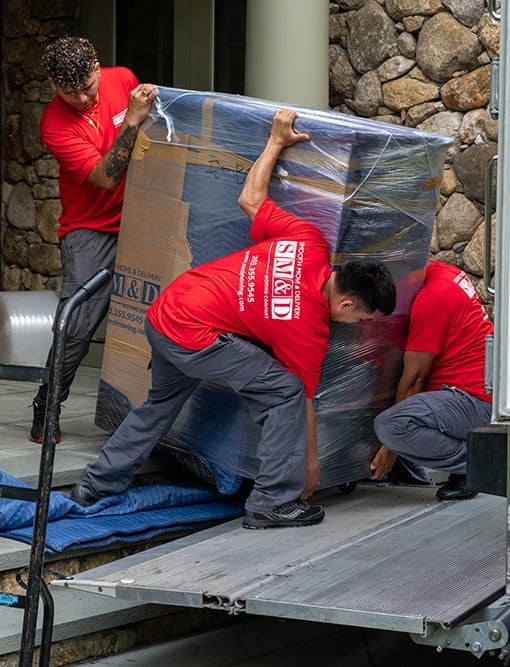 a big box is being loaded by three movers wearing red shirts and cargo pants onto a moving truck